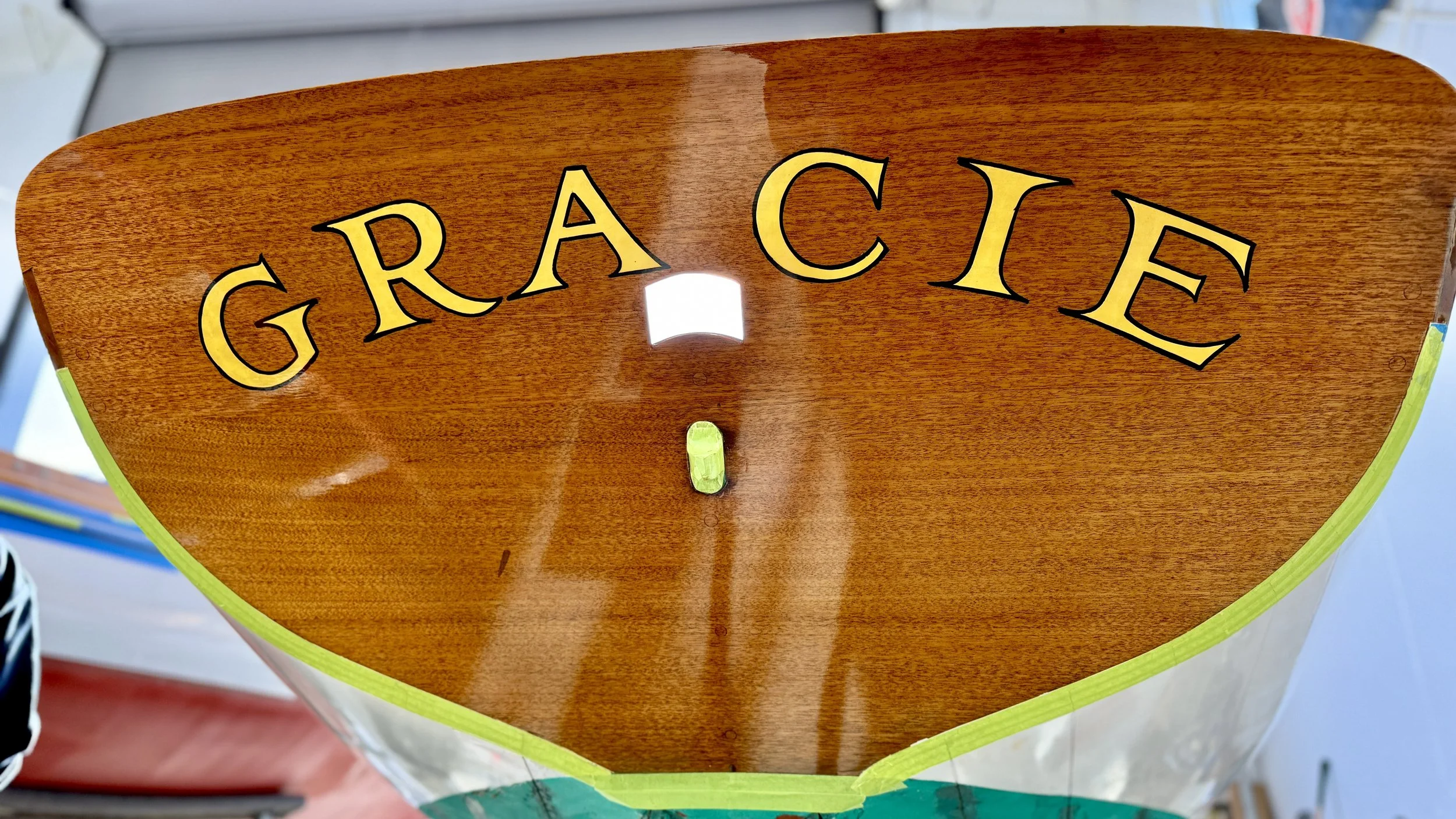 A close-up of a wooden sign with the word 'GRACE' in large yellow letters with black outline, mounted on a boat or similar wooden surface.