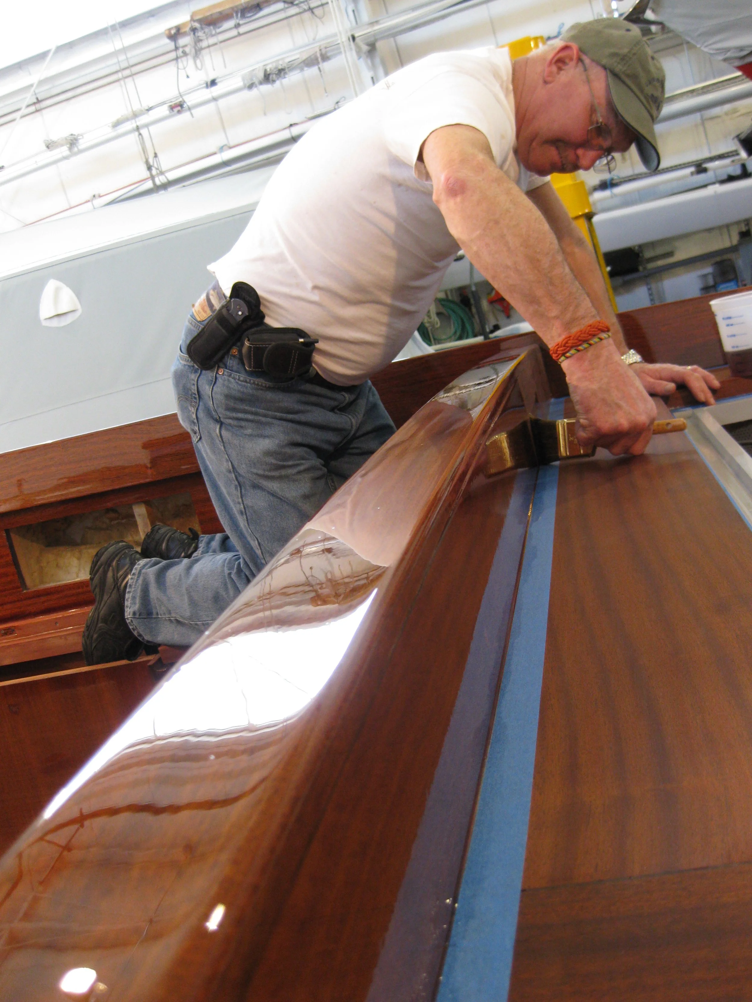 A man kneeling on a wooden surface working on a boat in a workshop.