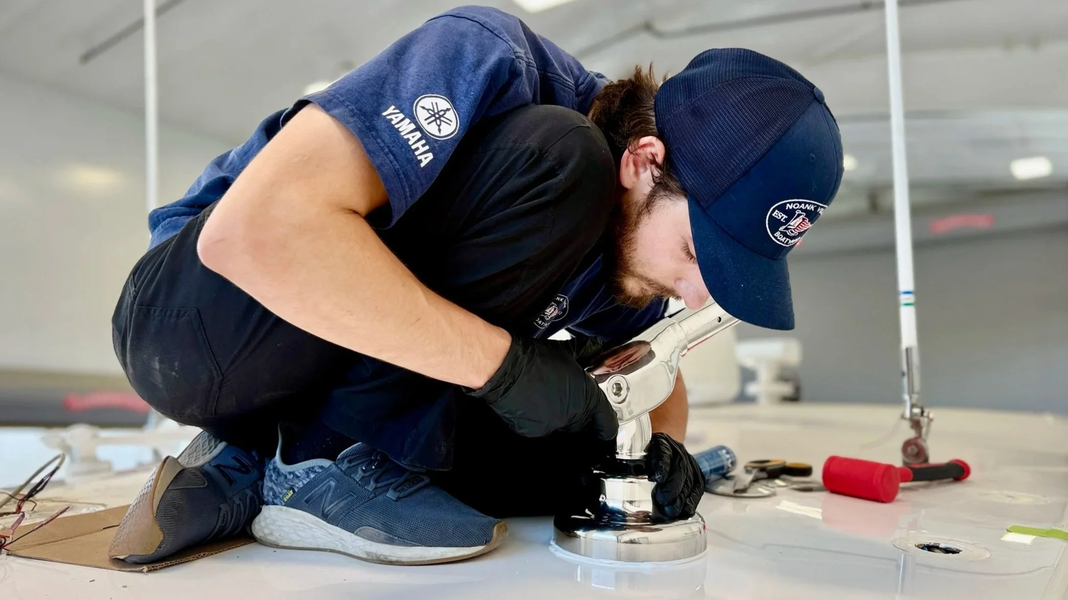 A technician wearing a blue Yamaha uniform and cap working on a boat propeller in a workshop.
