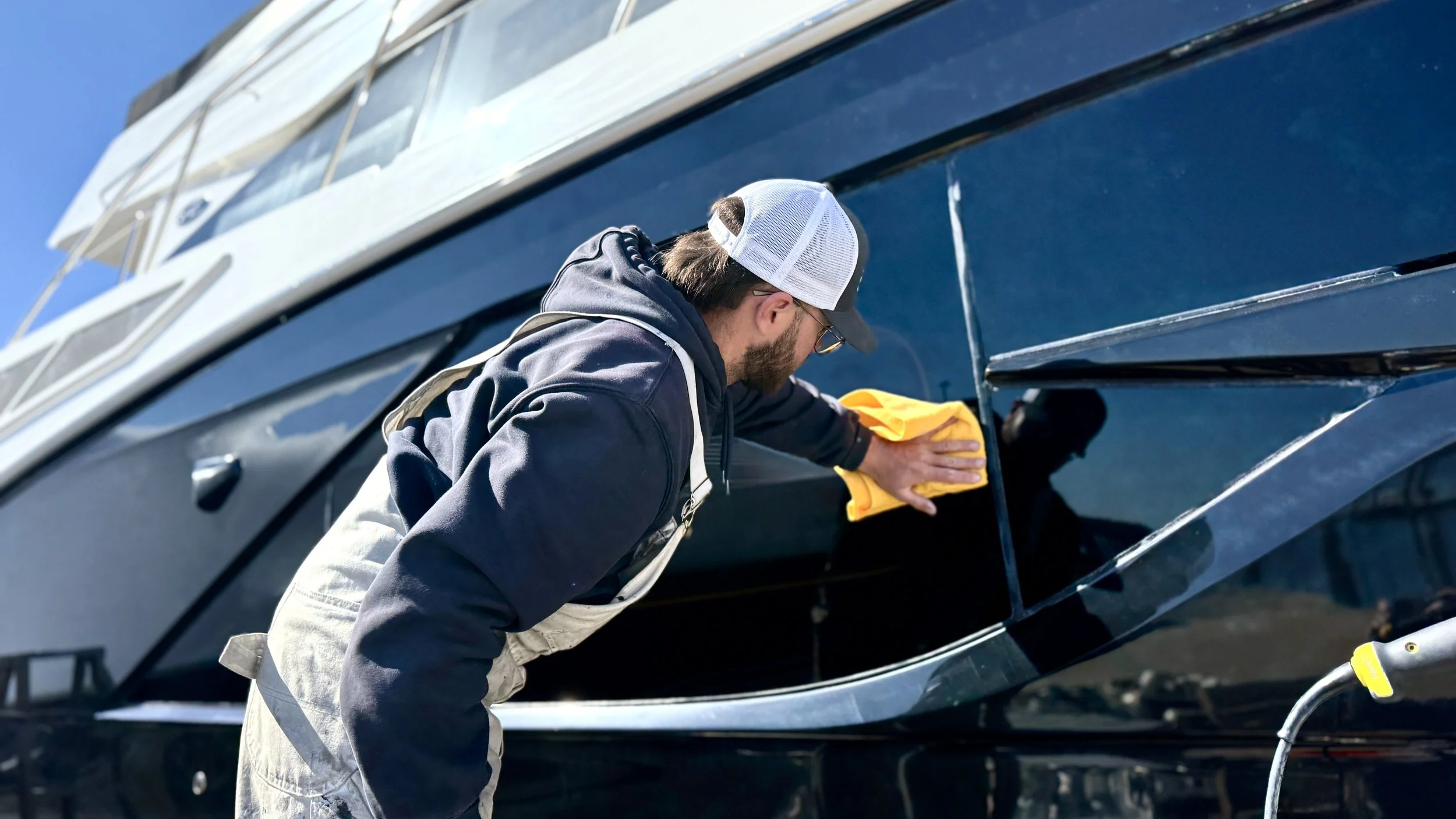 A man cleaning the exterior of a black boat with a yellow cloth.