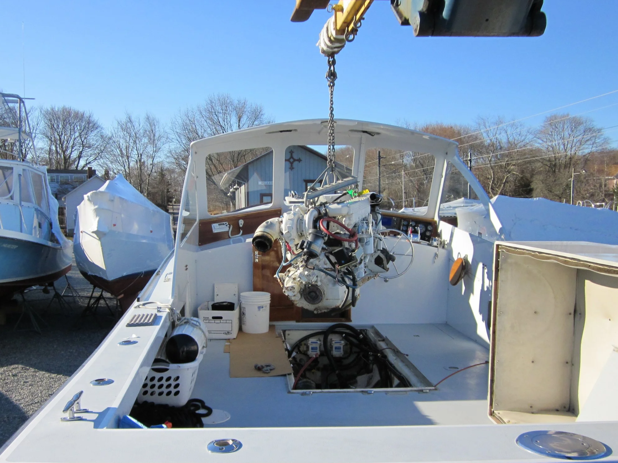 A boat under construction or maintenance, with parts and tools visible inside and outside. The boat's engine is exposed, and the surrounding area has other boats and boats' coverings.