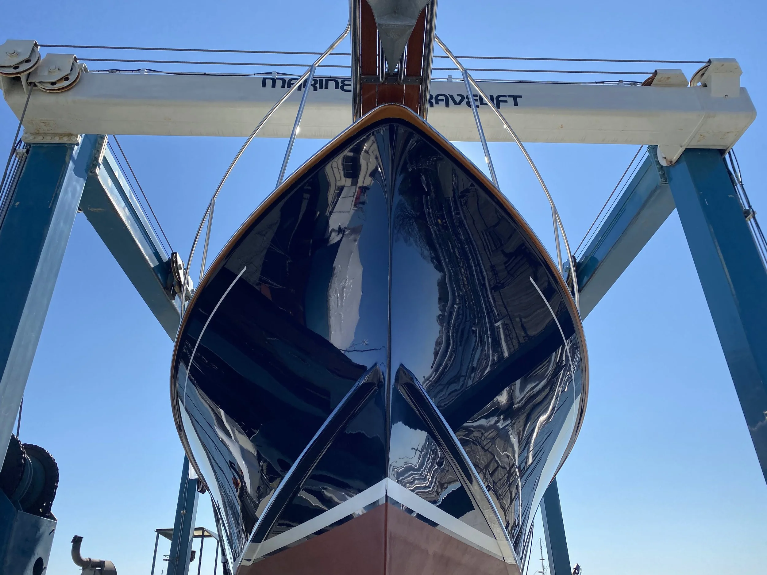 Close-up view of a boat hull under a boat lift with blue sky in the background.