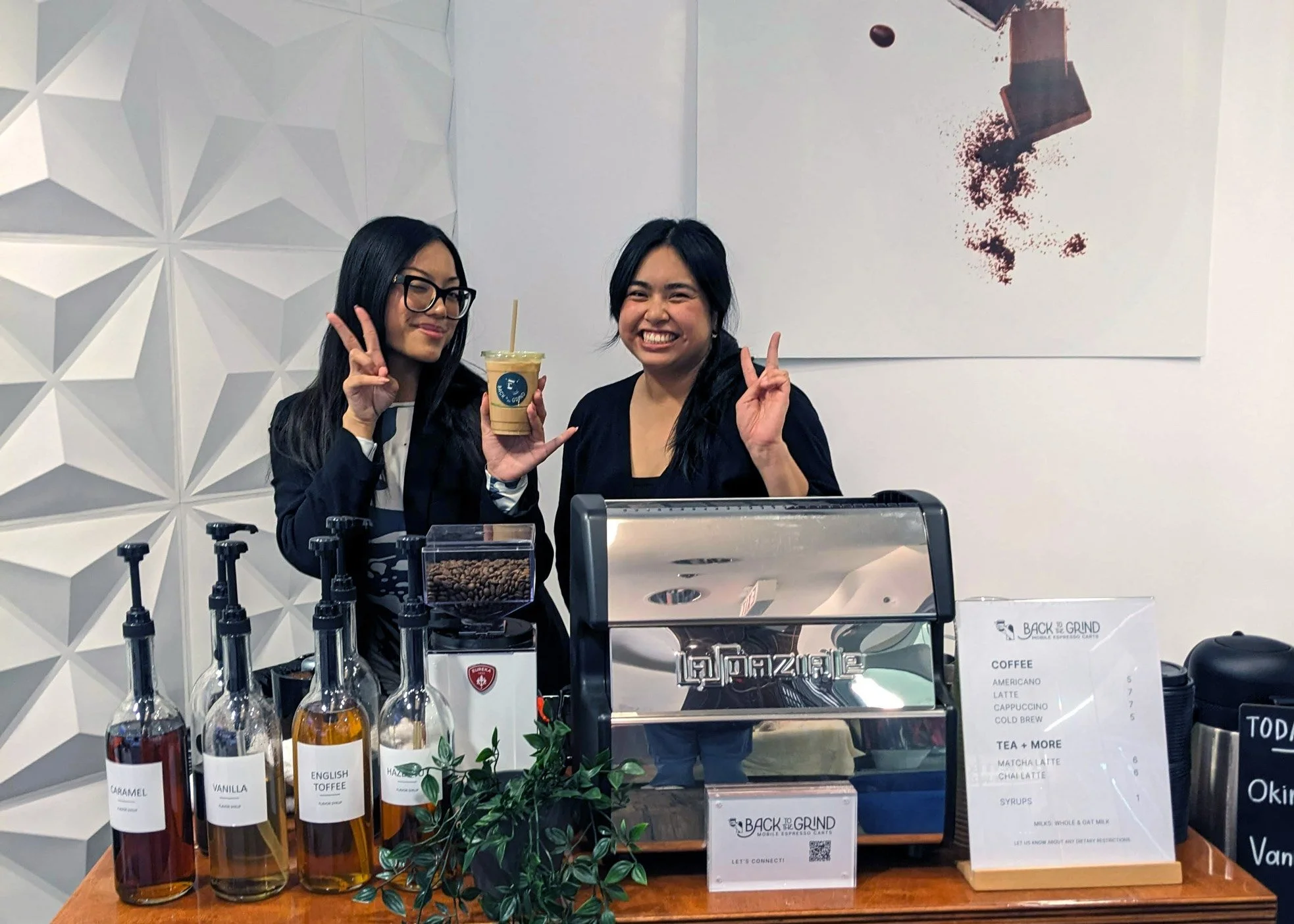 Two baristas showing peace signs behind the coffee cart