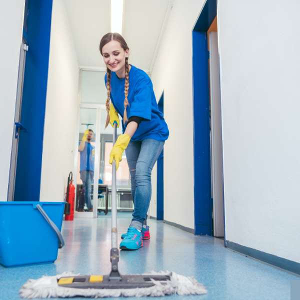 Young woman cleaning the floor with a mop in a hallway, wearing yellow gloves and casual clothes, smiling.