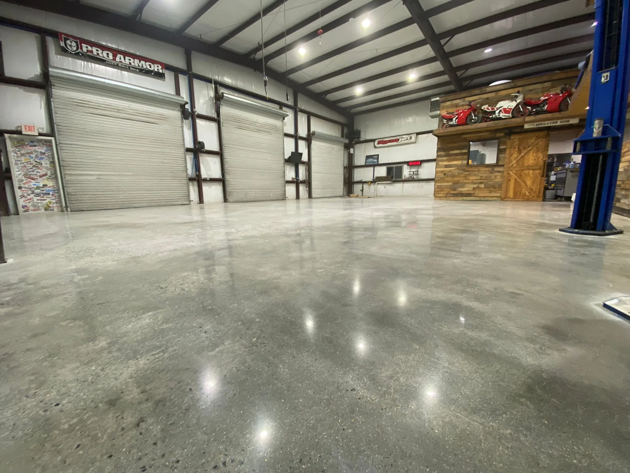 Inside an empty warehouse with roller doors, a wooden platform with red and white motorcycles, and a display case with stickers.