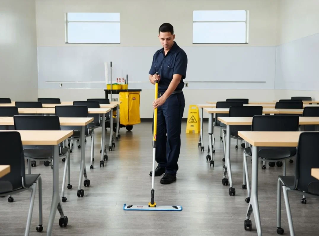 A janitor in a classroom mopping the floor.