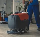 A person operating a floor cleaning machine in an indoor setting.