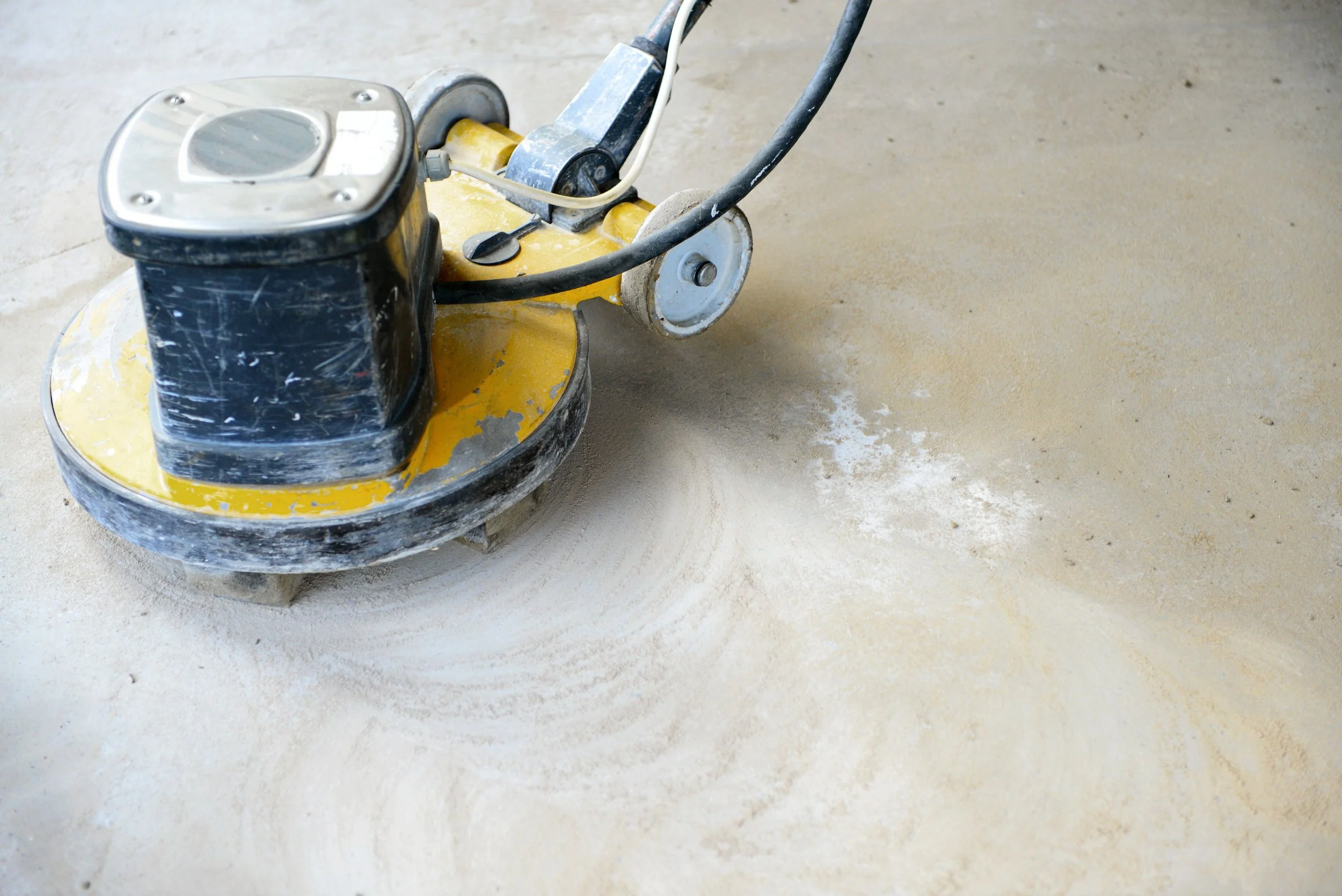 A yellow and black floor polishing machine on a light concrete floor.