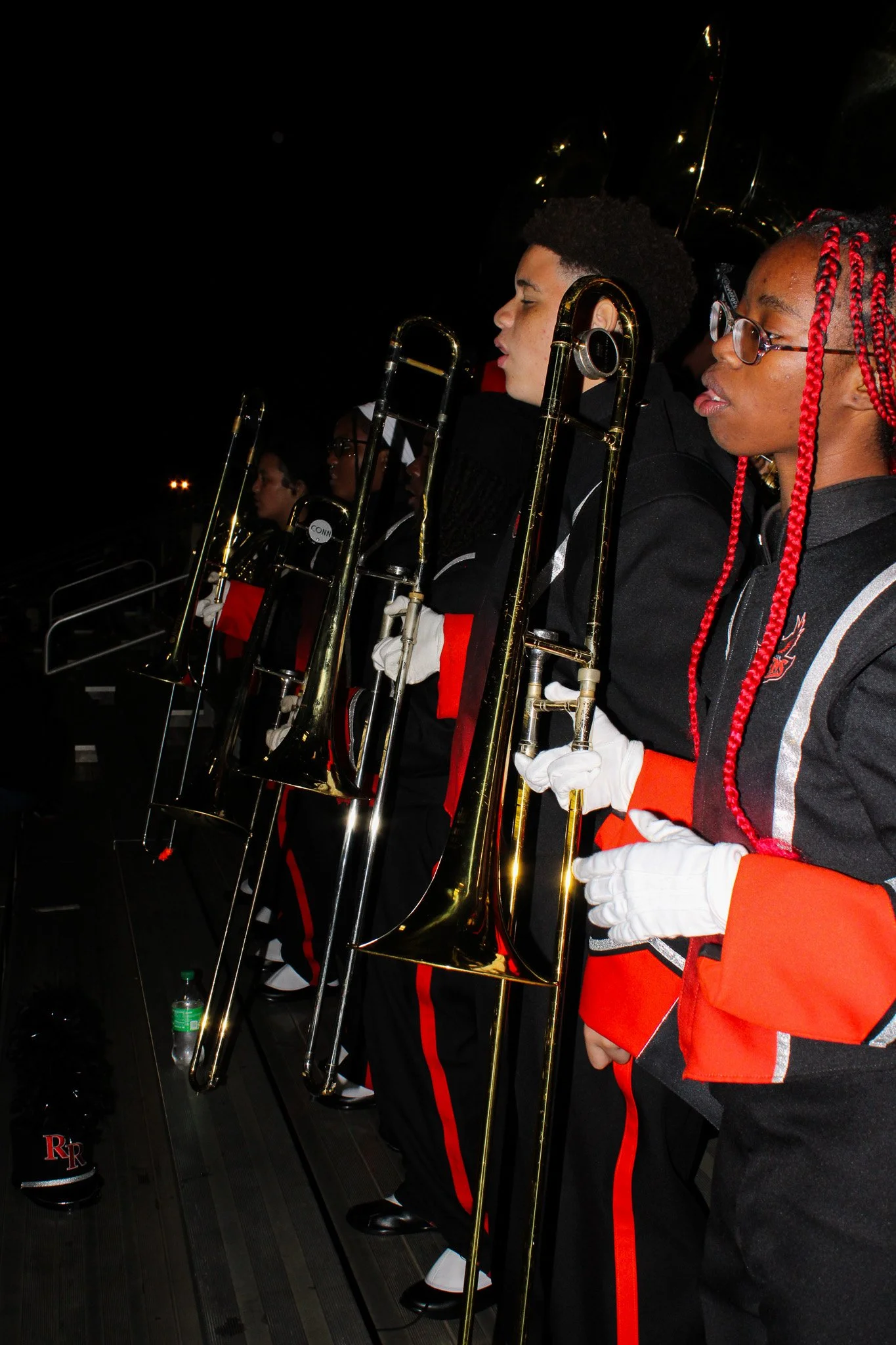 Band members in marching band uniforms holding brass instruments during a performance at night.