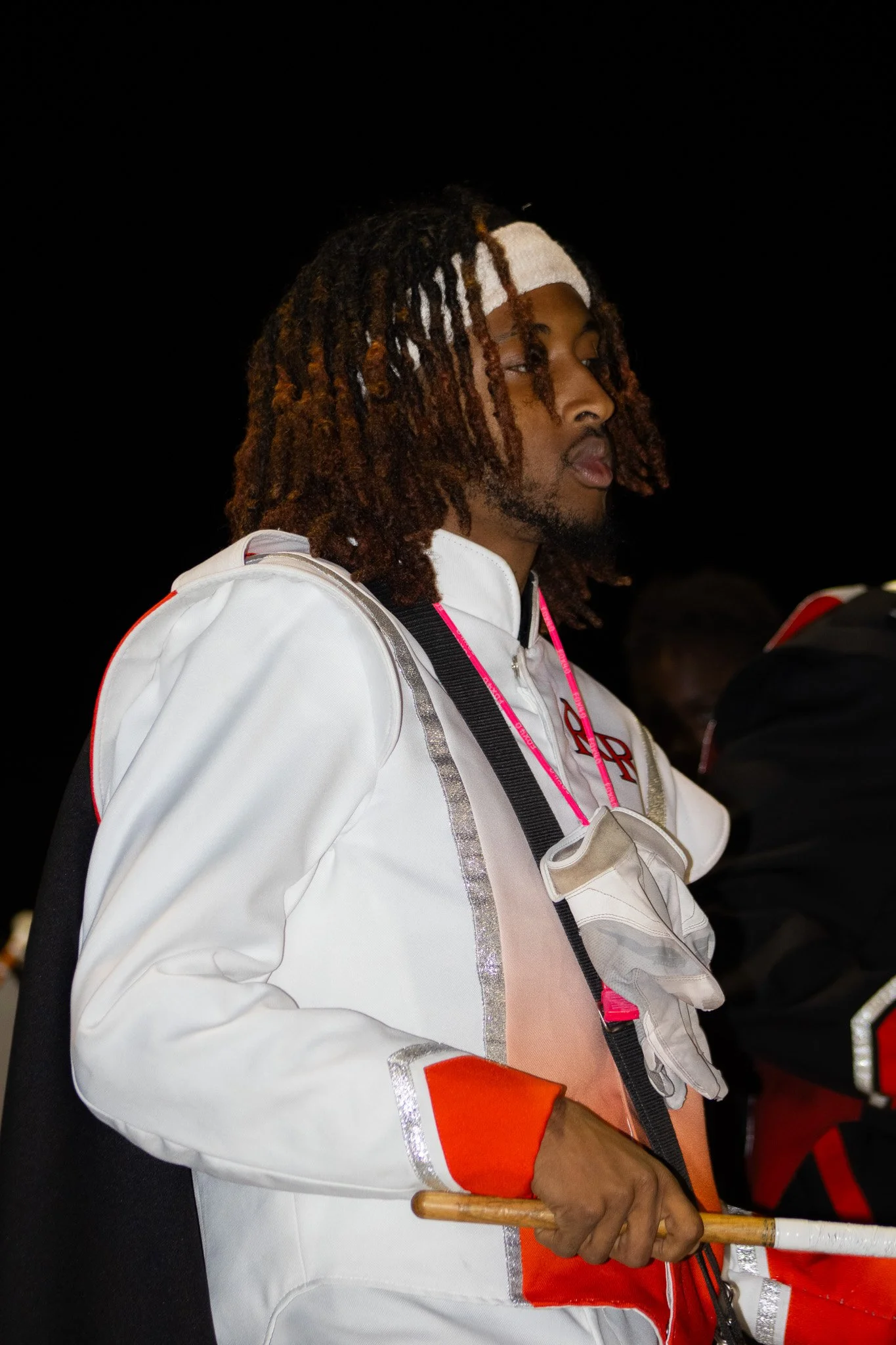 Man in white sports jacket with red accents holding a baton, standing outdoors at night.