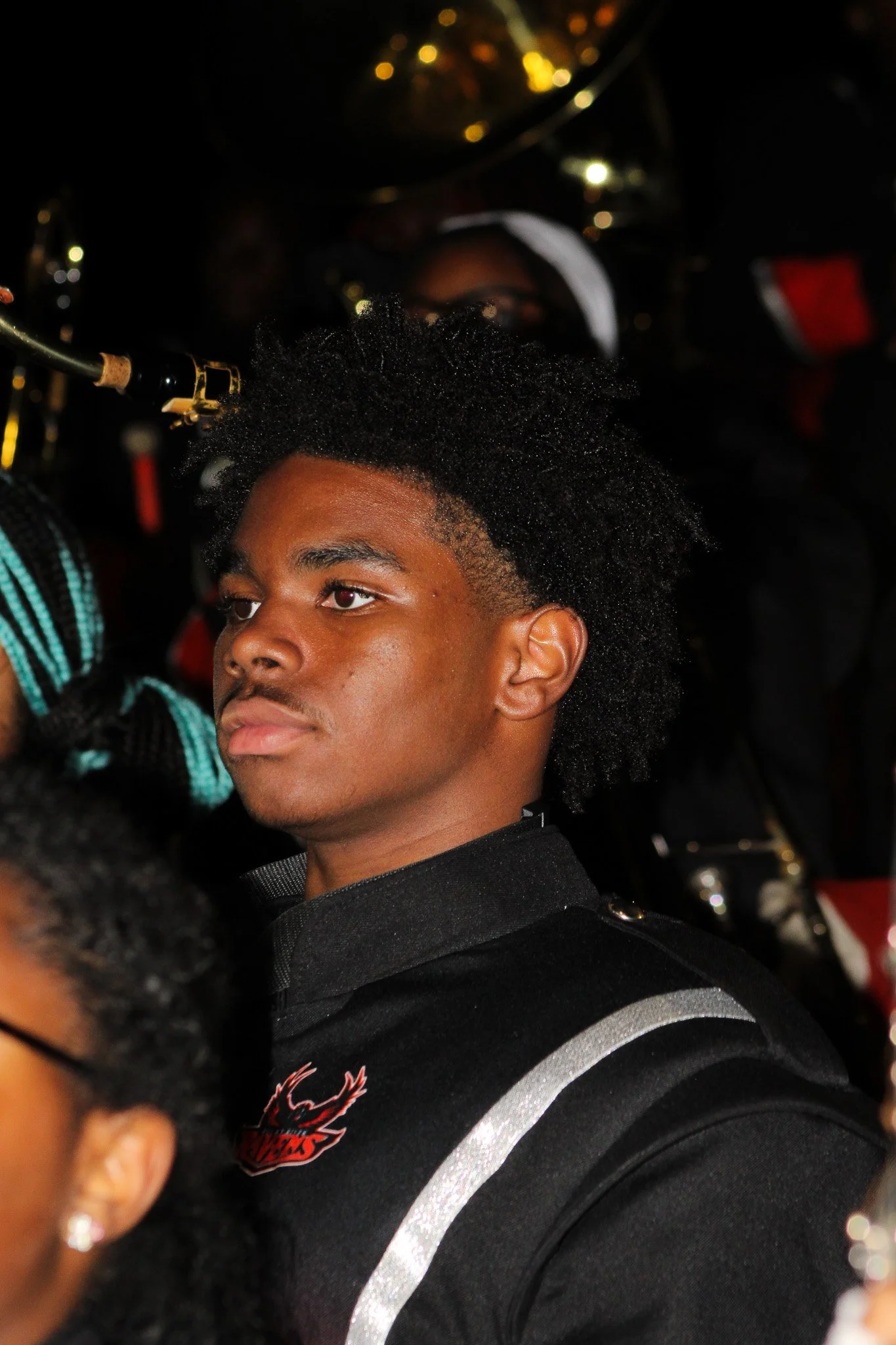 Young man with a styled afro wearing a black shirt with reflective stripes, in a crowd at night.
