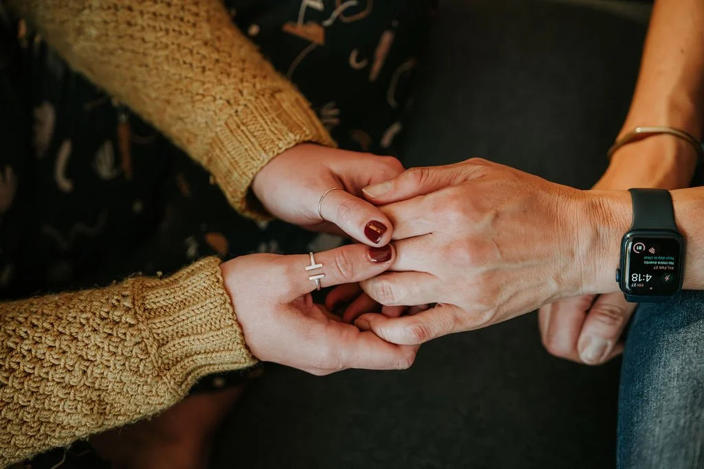 Two people holding hands, one wearing a knitted brown sweater and the other wearing a watch and a bracelet.