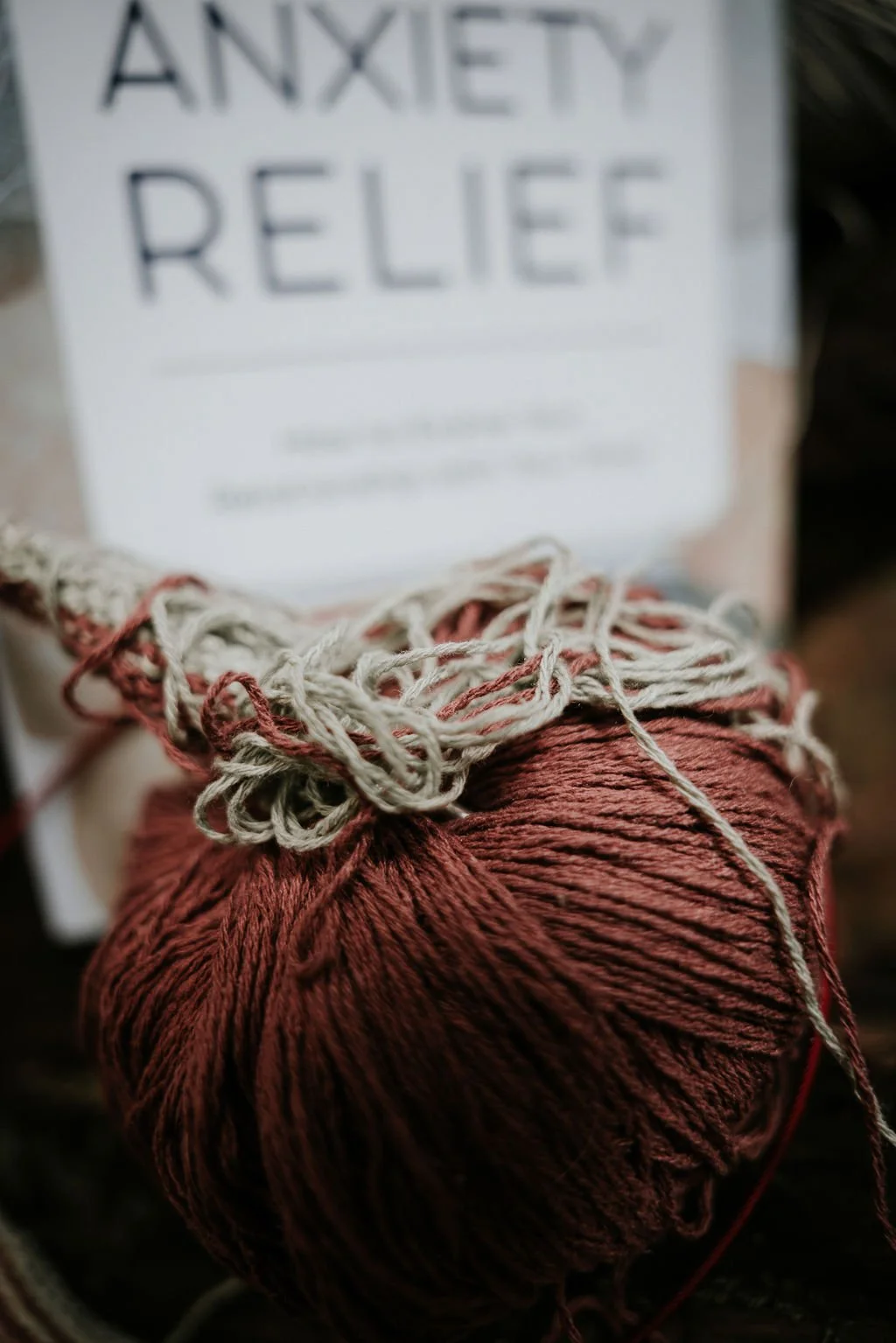 A ball of red yarn with white and red strings on top. In the background, there is a blurred sign that reads 'Anxiety Relief'.