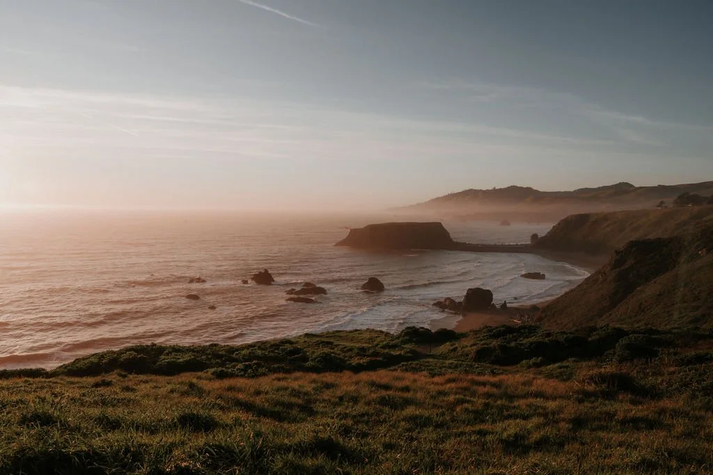 Coastal landscape with cliffs, rocky shoreline, and ocean during sunset or sunrise.