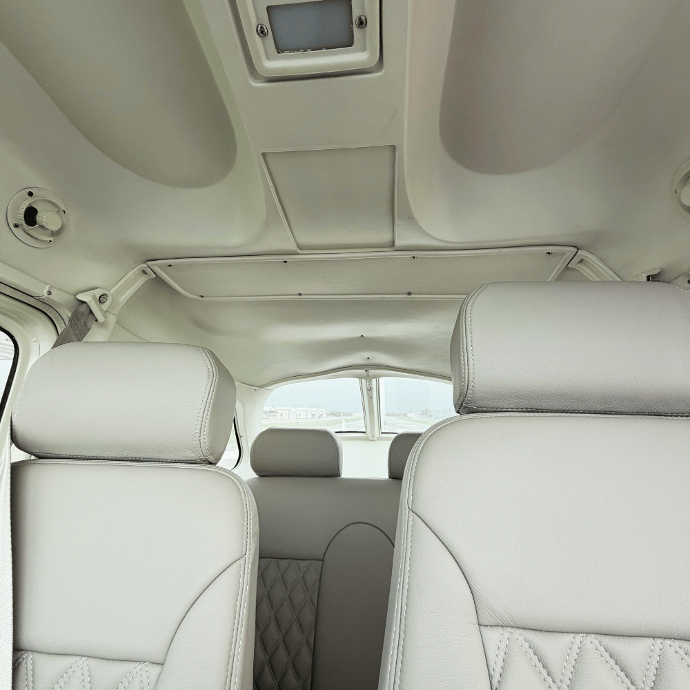 Interior of a light-colored vehicle with headrests, windows, and ceiling details visible.
