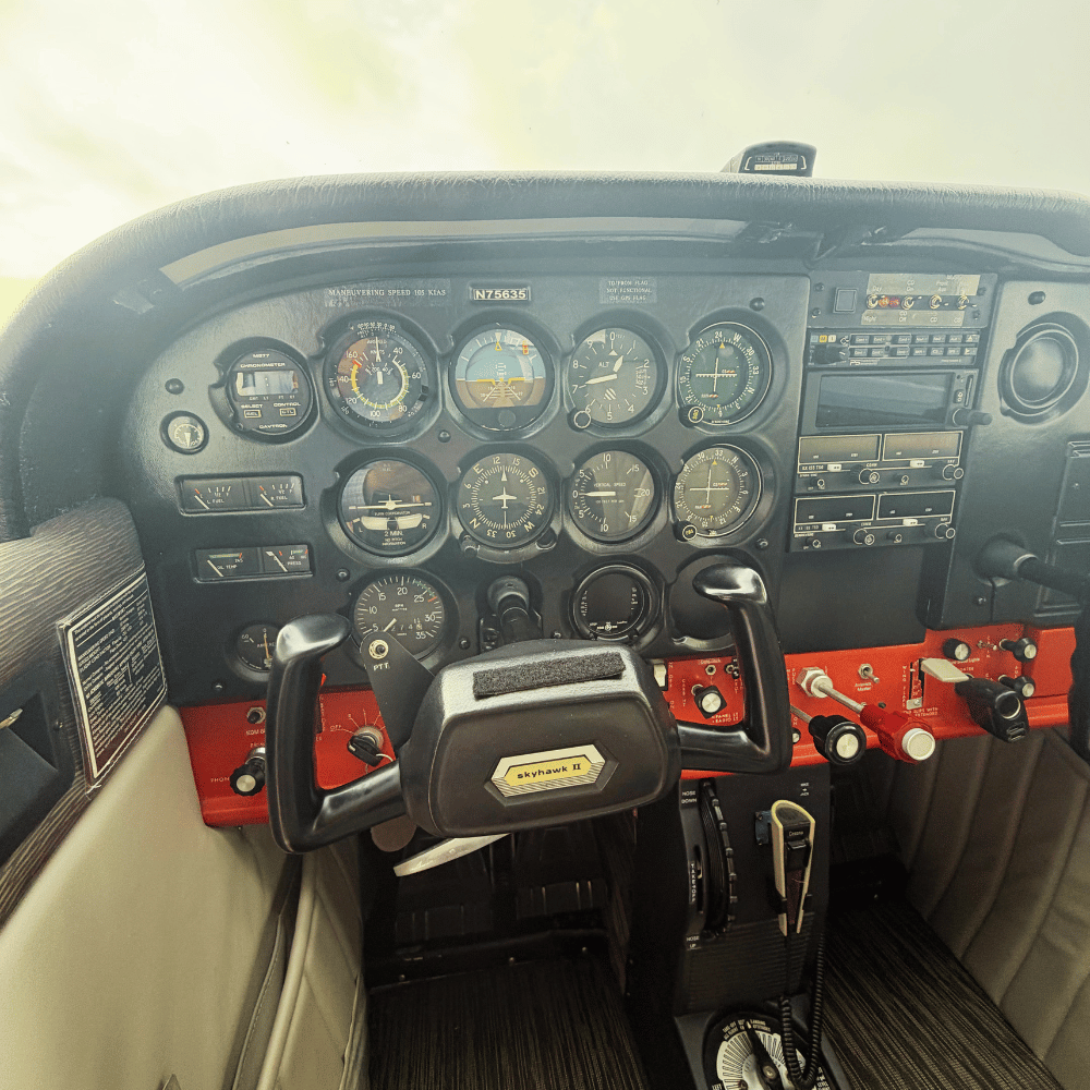 The cockpit of a small aircraft with various gauges, controls, and a throttle, including a yoke labeled 'Skyhawk II.'