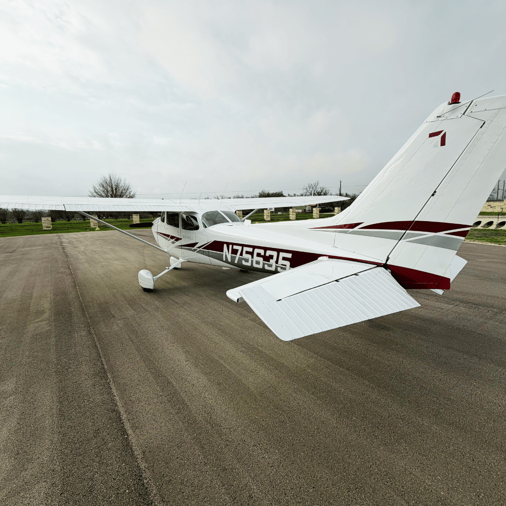 A small white airplane with red accents parked on a paved surface at an airfield under a cloudy sky.