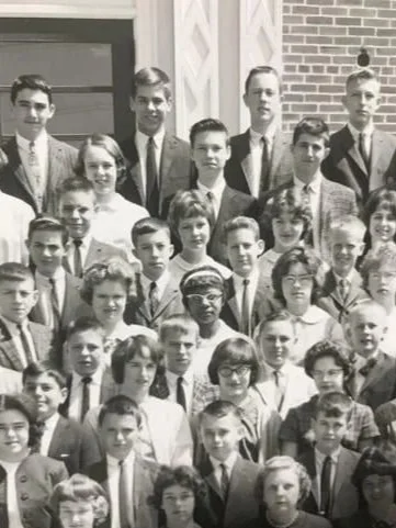 Black and white photo of a large group of children and a few adults standing in front of a brick building.