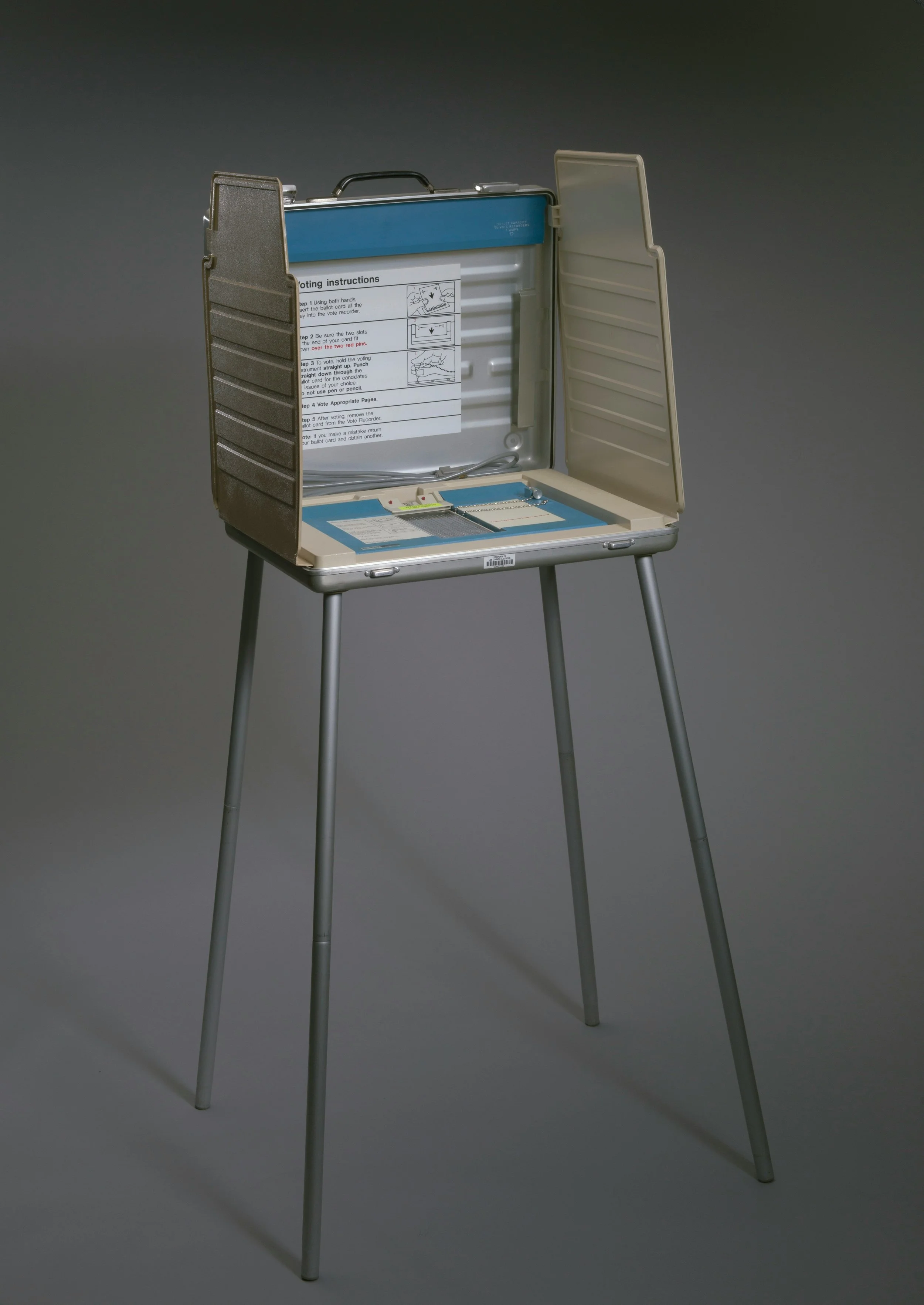 A portable voting machine with a stand, open to reveal instructions and internal components, set against a neutral background.