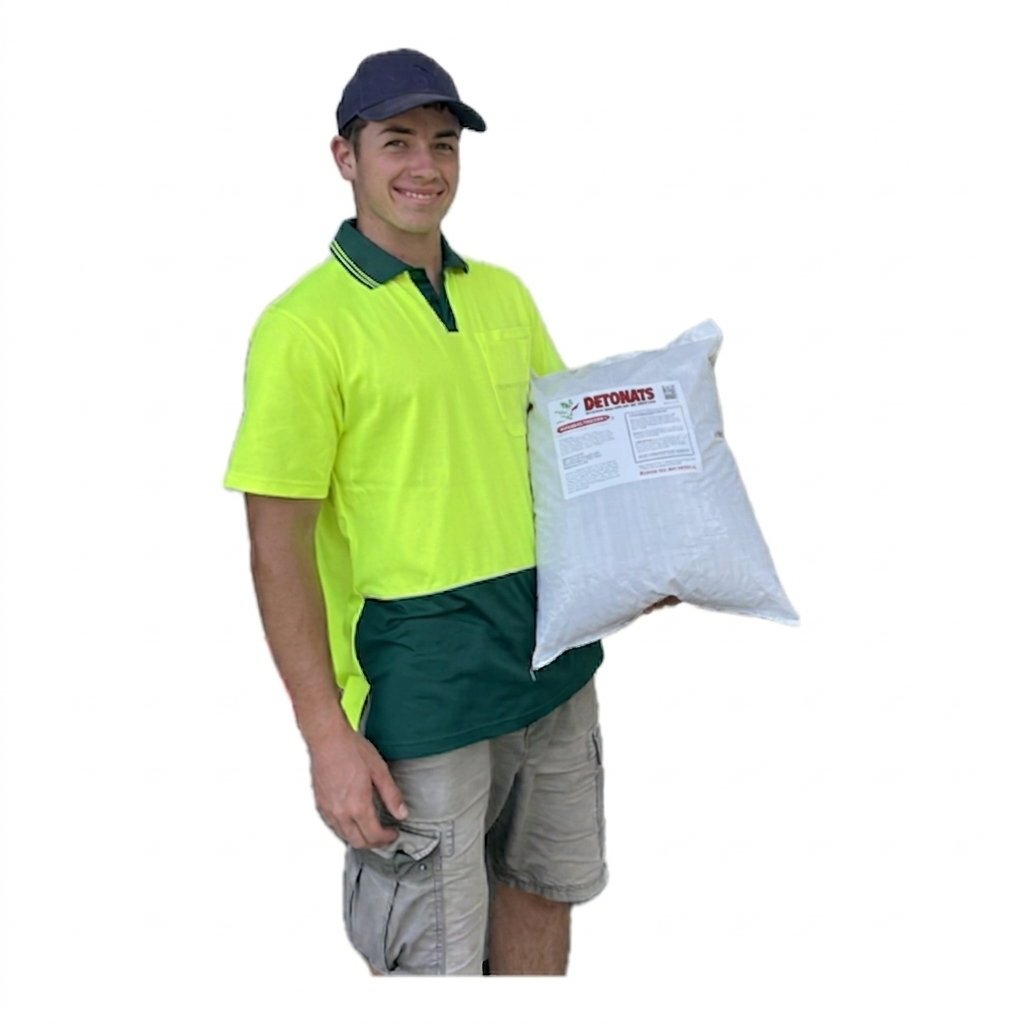 A young man wearing a blue cap, yellow safety shirt, and beige cargo shorts, holding a large bag ofDetonats. The background is plain white.