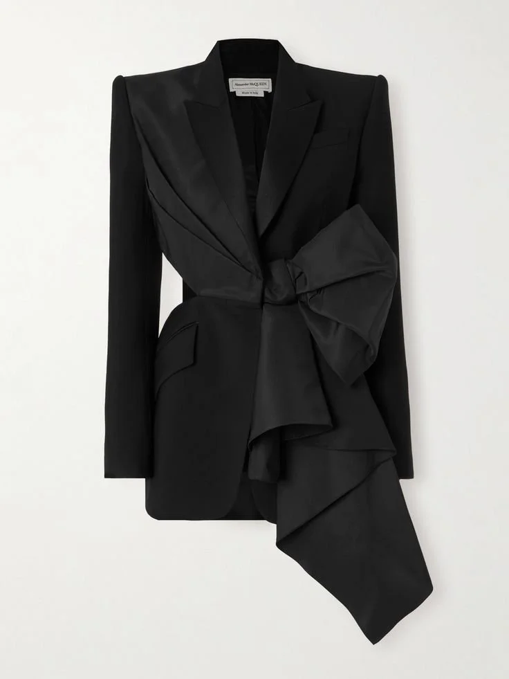 Black tailored blazer with large decorative bow and fabric draping on a white background.