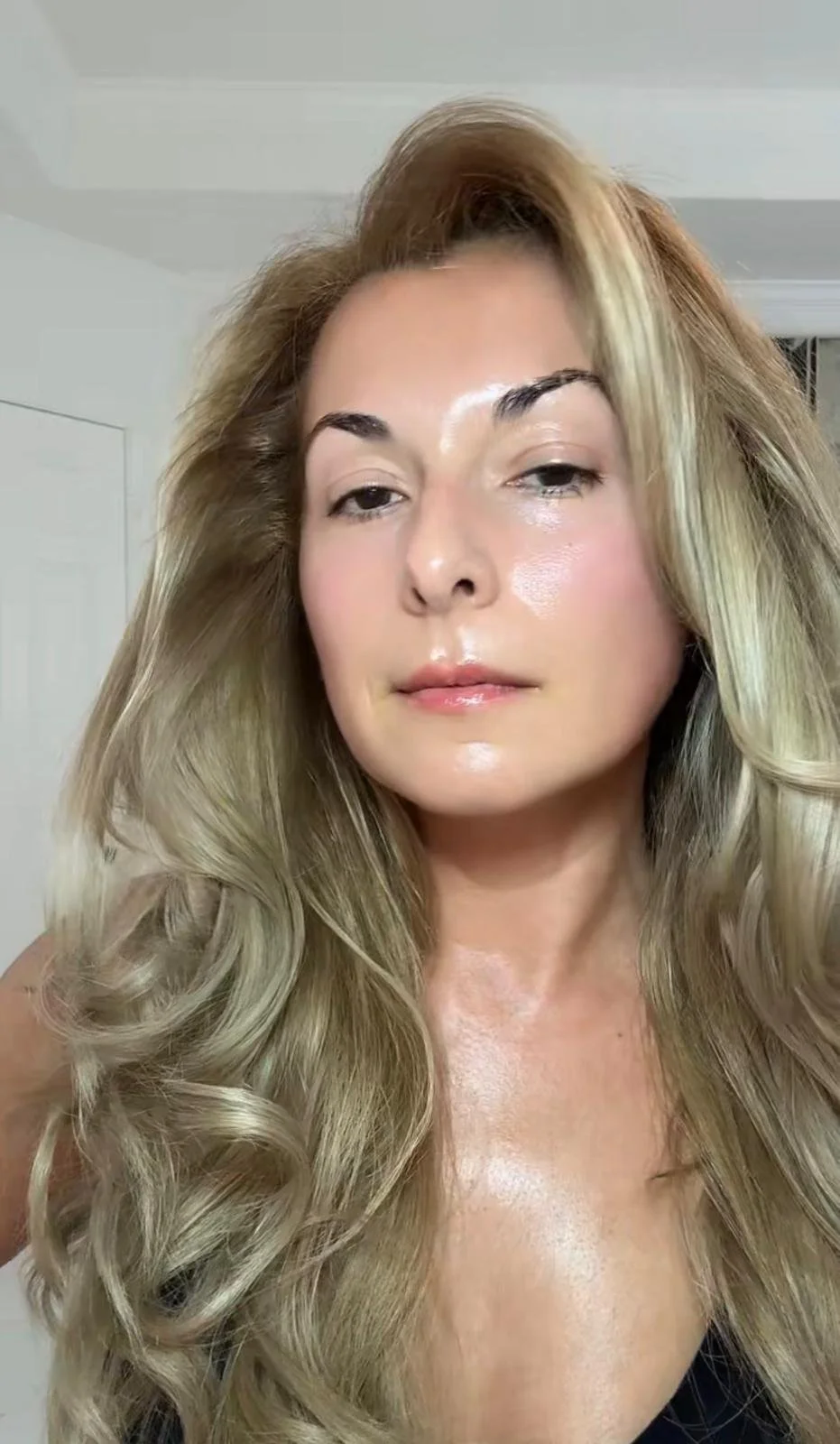 Close-up of a woman with long, wavy blonde hair and a confident expression.