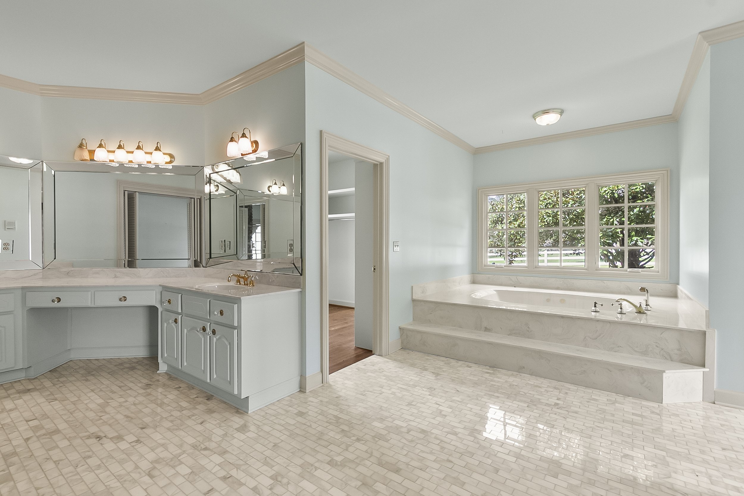 Bathroom with a large bathtub near a window, a light blue vanity with a mirror, and tiled floors.