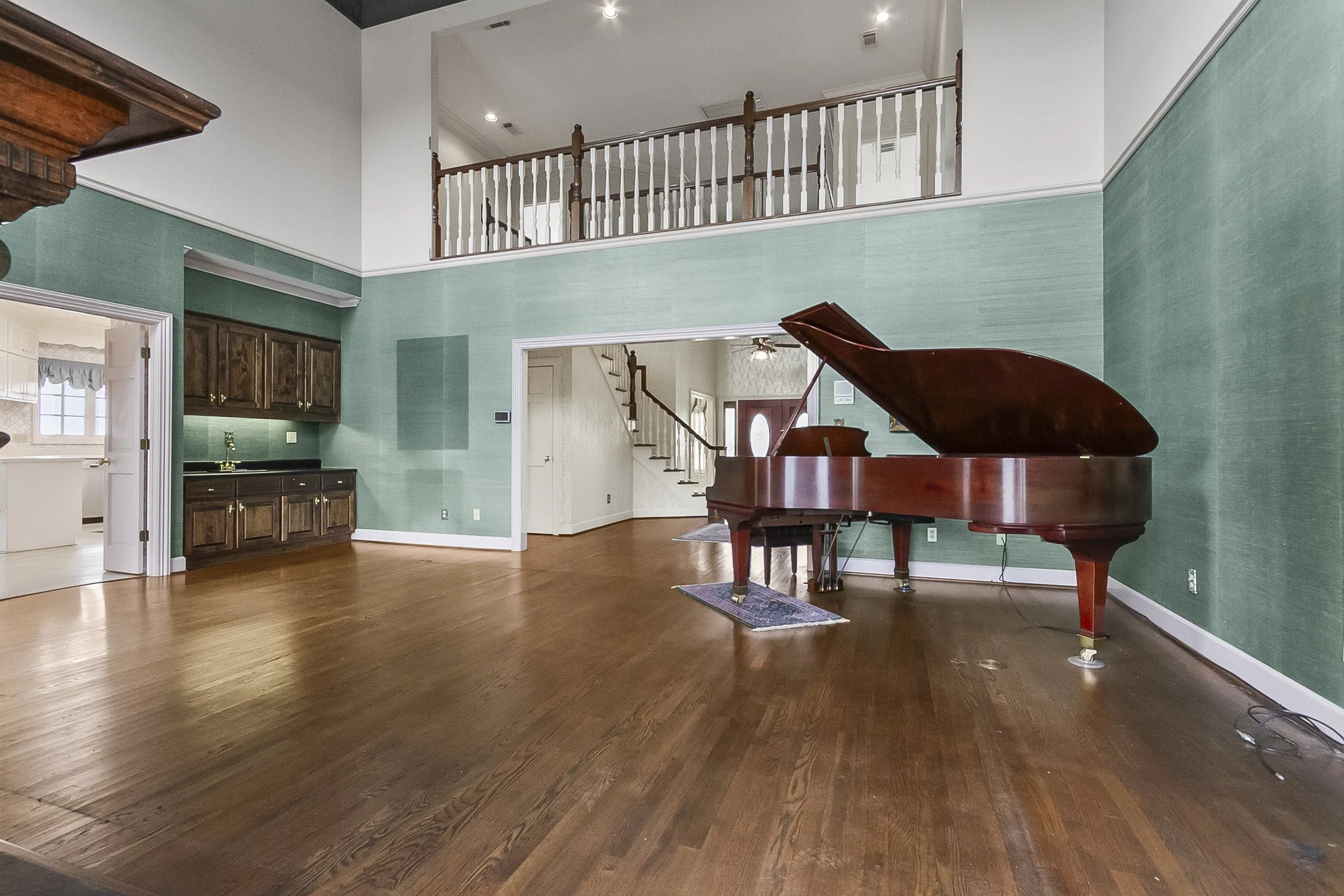 Interior of a house with hardwood floors, green walls, a grand piano, staircase, and upper balcony.