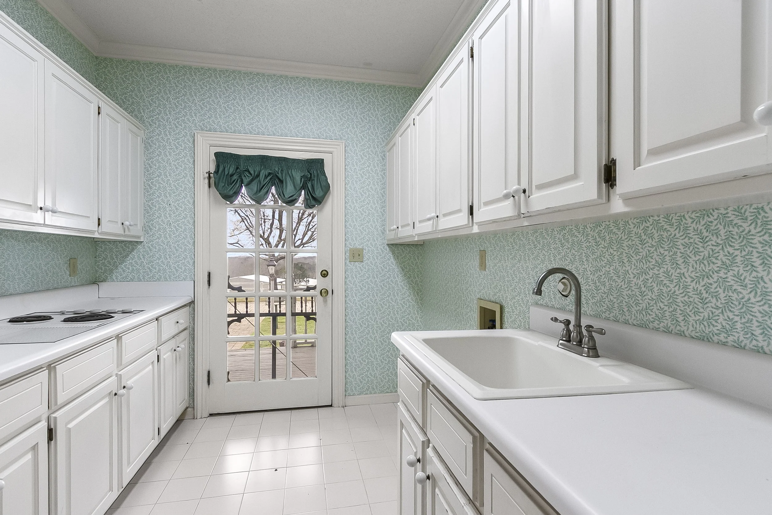 Kitchen with white cabinets, a sink, stove, and a door leading outside.