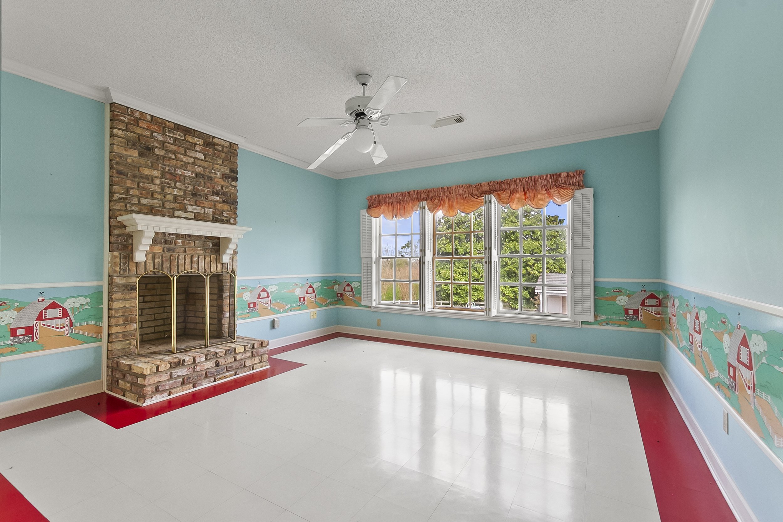 Room with light blue walls, a brick fireplace with a white mantel, a large window with white shutters, a pink valance, and a painted mural of a farm scene along the lower wall. The floor is white with a red border.