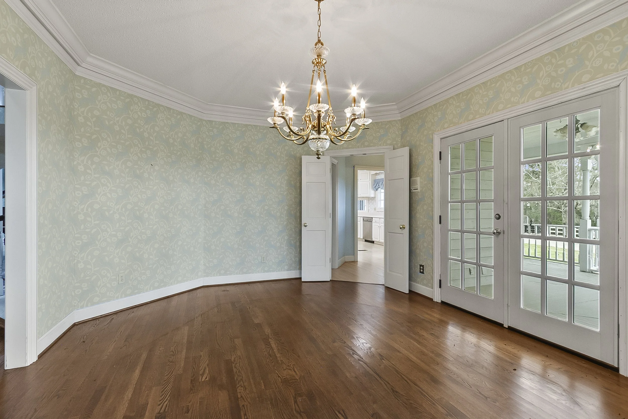 Empty living room with hardwood floors, a chandelier, and glass double doors leading to a porch.