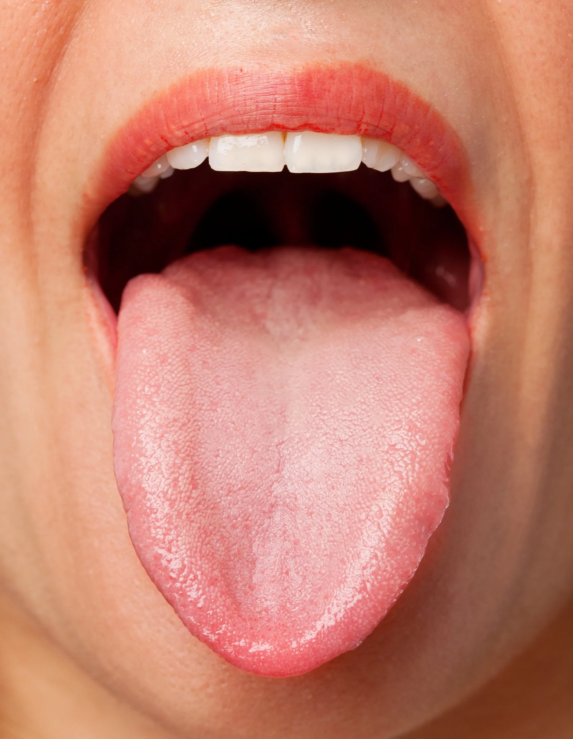Close-up of a person's open mouth showing white teeth, pink lips with red lipstick, and their tongue sticking out.