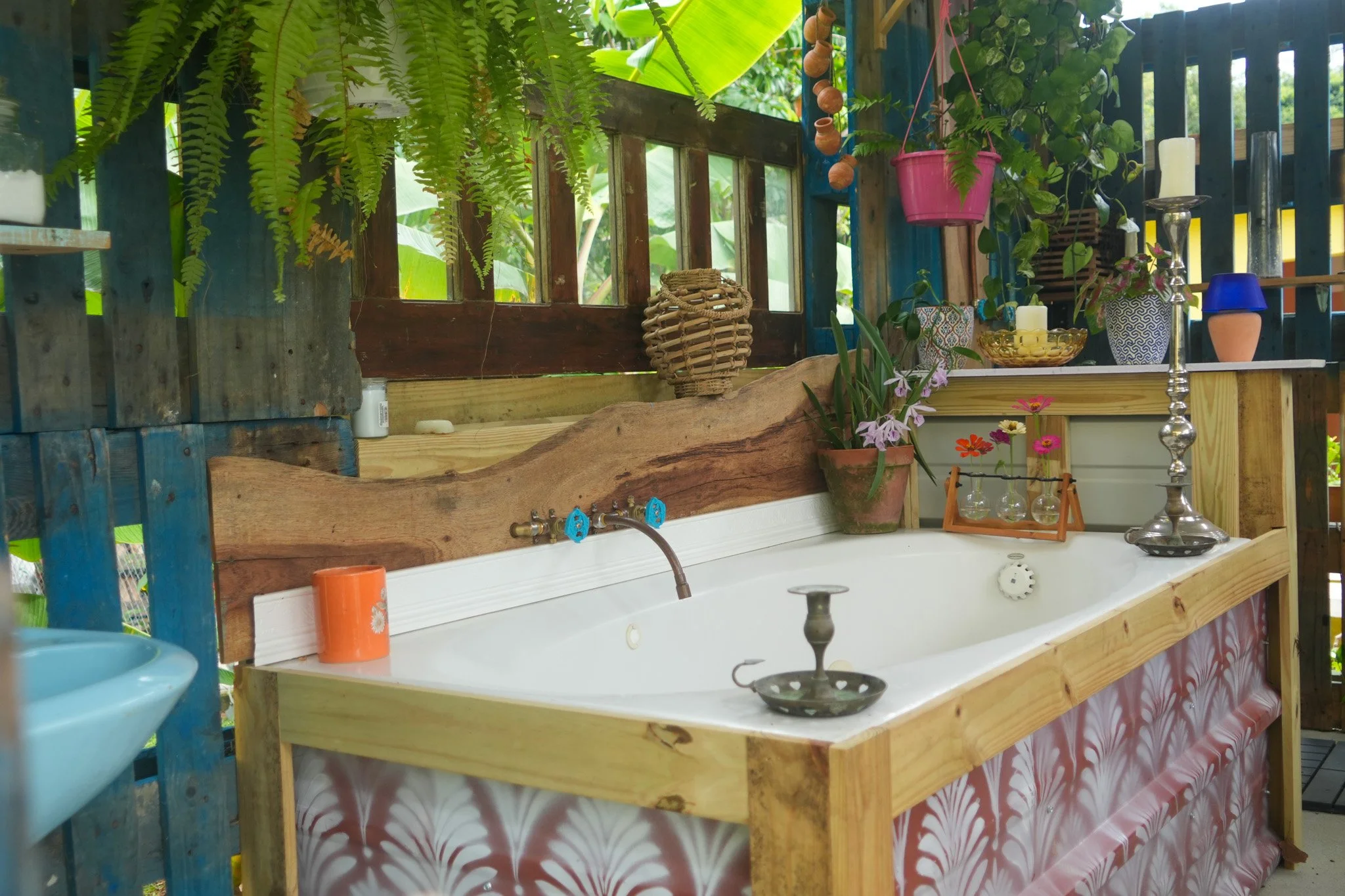 Indoor garden with wooden and colorful decor, plants, hanging pots, and a white sink with plants and decorative items on the countertop.
