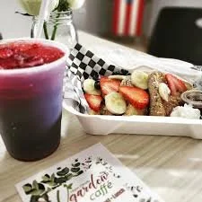 A glass of red and purple fruit smoothie next to a basket of French toast topped with strawberries and bananas, with syrup on the side, on a table at a cafe.