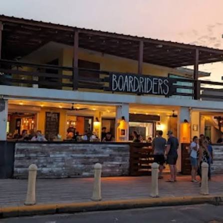A two-story building named 'Boardriders' with people outside and inside, at dusk.