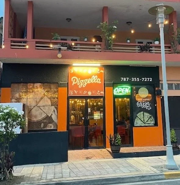 Pizza restaurant named Pizzella with a bright orange sign, green 'Open' sign, and glass doors, located on a city street.