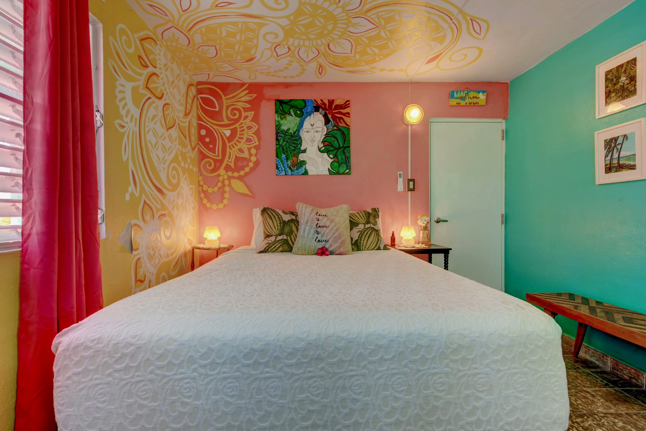 A colorful bedroom with yellow, pink, and teal walls, featuring a bed with a white quilt and pillows, colorful artwork on the walls, pink curtains, and bedside lamps.
