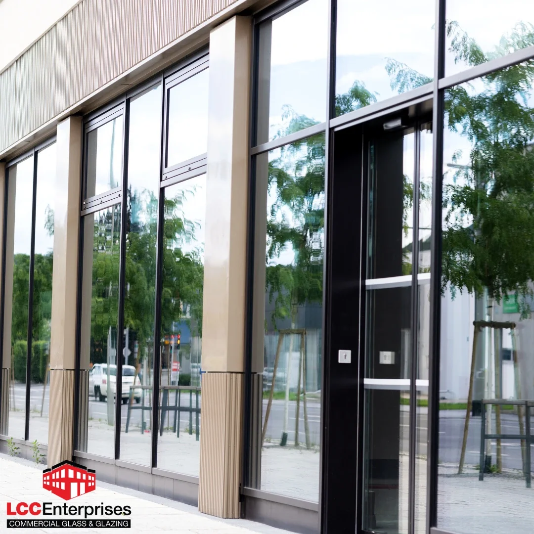 The exterior facade of a commercial building in Virginia featuring dark bronze aluminum-framed storefront glazing with large reflective glass panels, a glass entrance door with hardware, and wood-panel cladding accents on a clear day
