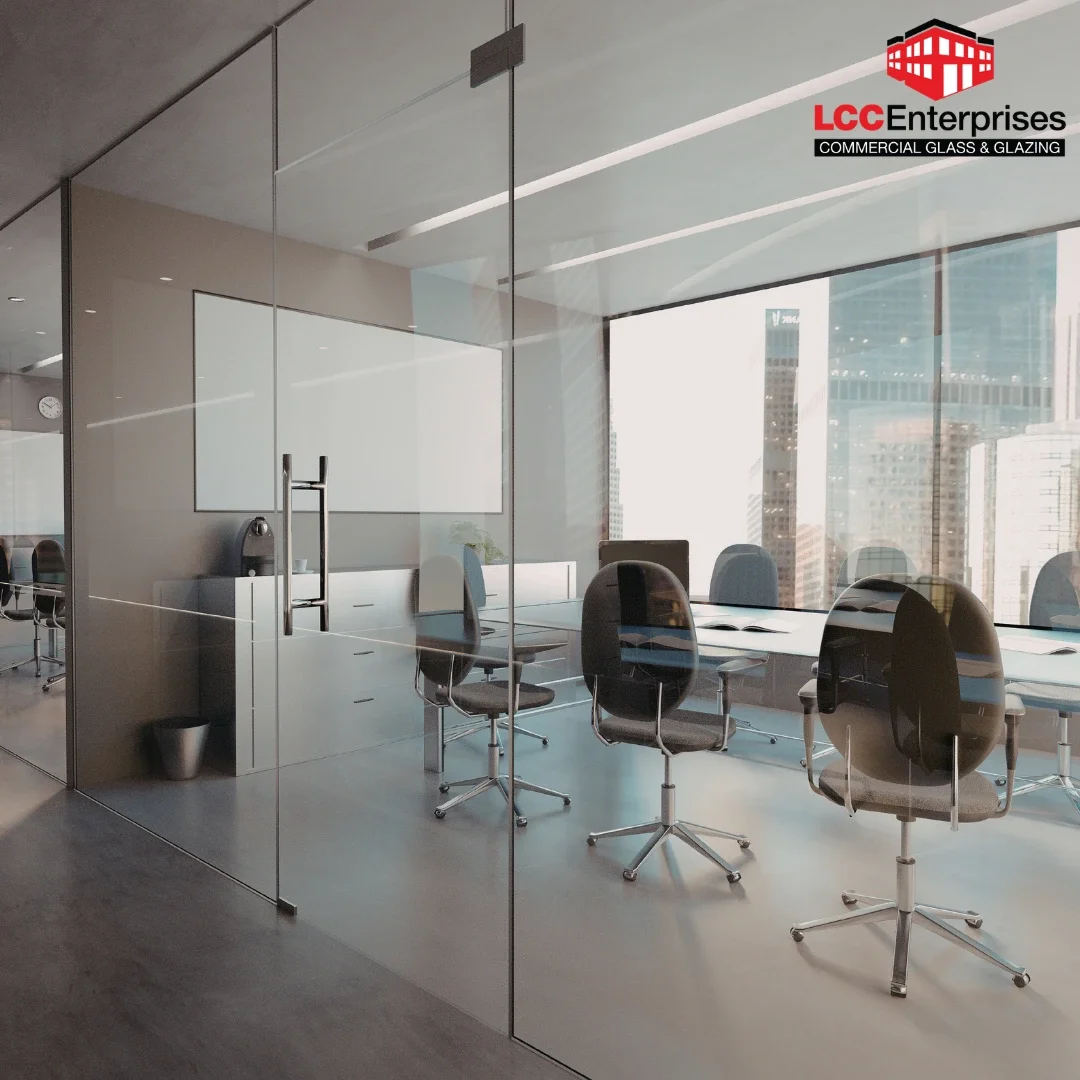 A modern commercial office interior in Virginia featuring floor-to-ceiling frameless glass partition walls with aluminum pull hardware, a conference table with ergonomic chairs, and a city skyline visible through exterior windows
