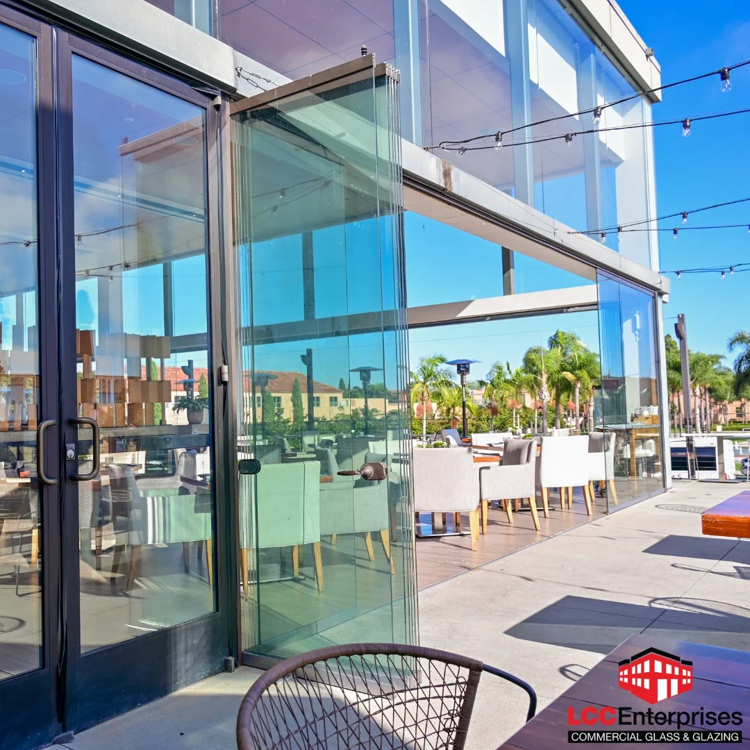 The exterior of a commercial building in Virginia showing a large aluminum-framed storefront glazing system with glass doors, folding glass panels, and an outdoor patio seating area under string lights on a clear day