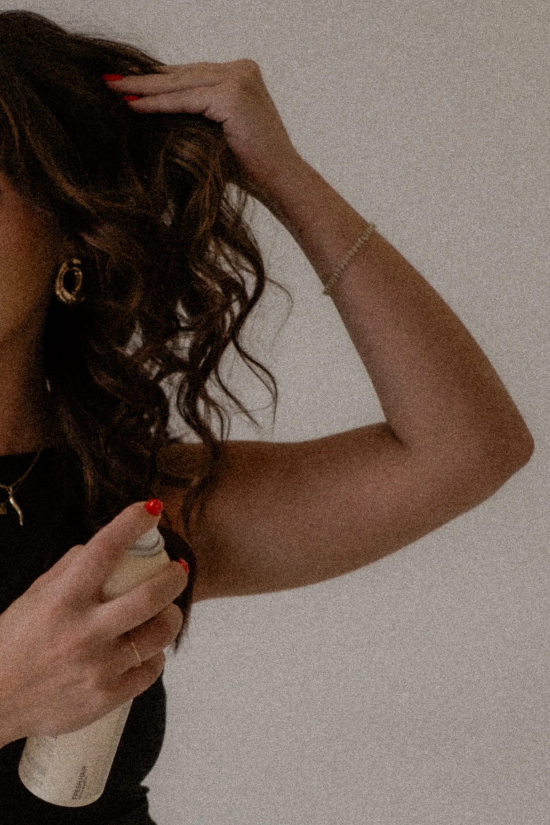 A woman with curly hair is spraying deodorant on her armpit.