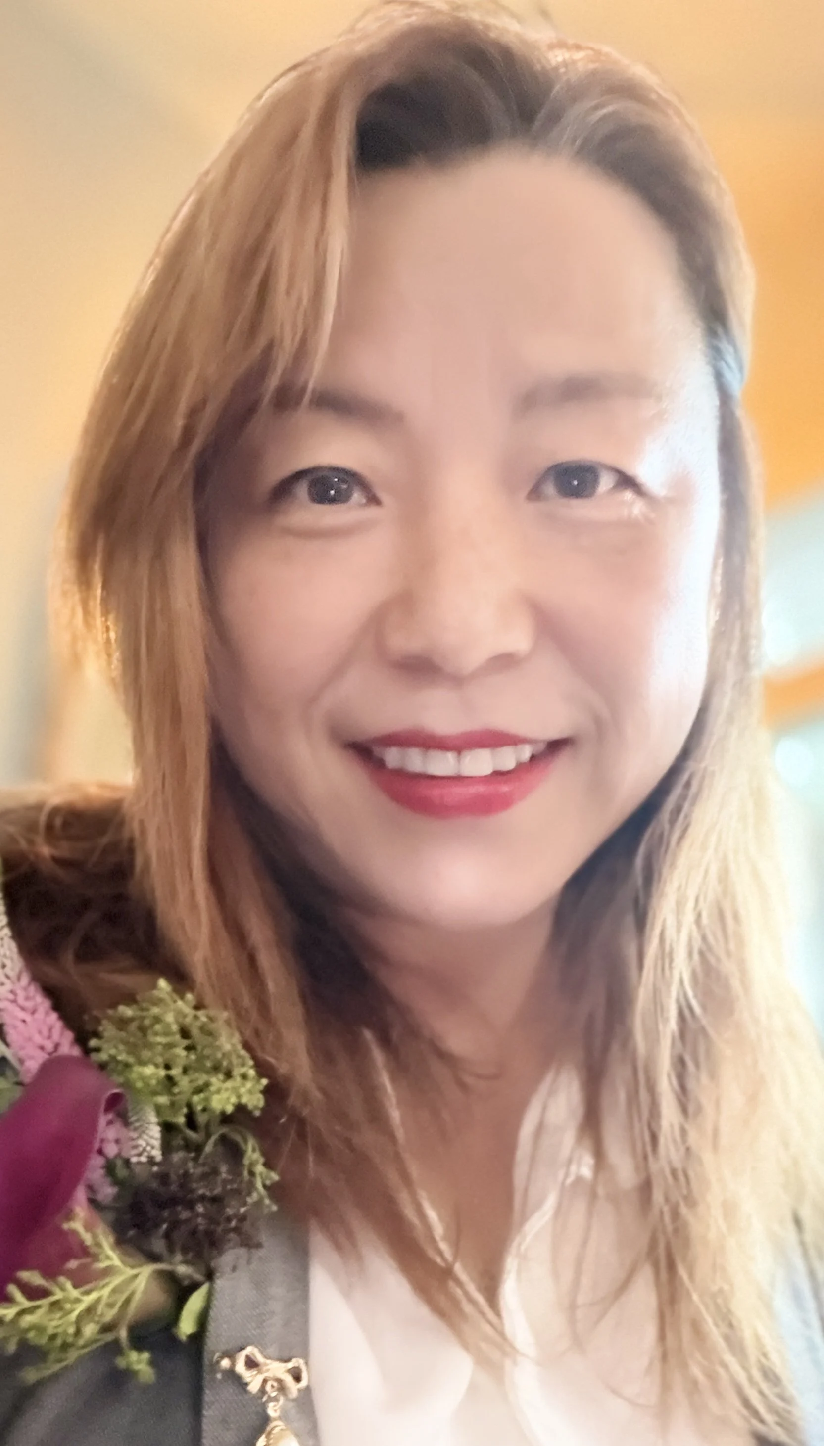 A woman smiling with long light brown hair, wearing a black and white outfit, and holding a bouquet of flowers.