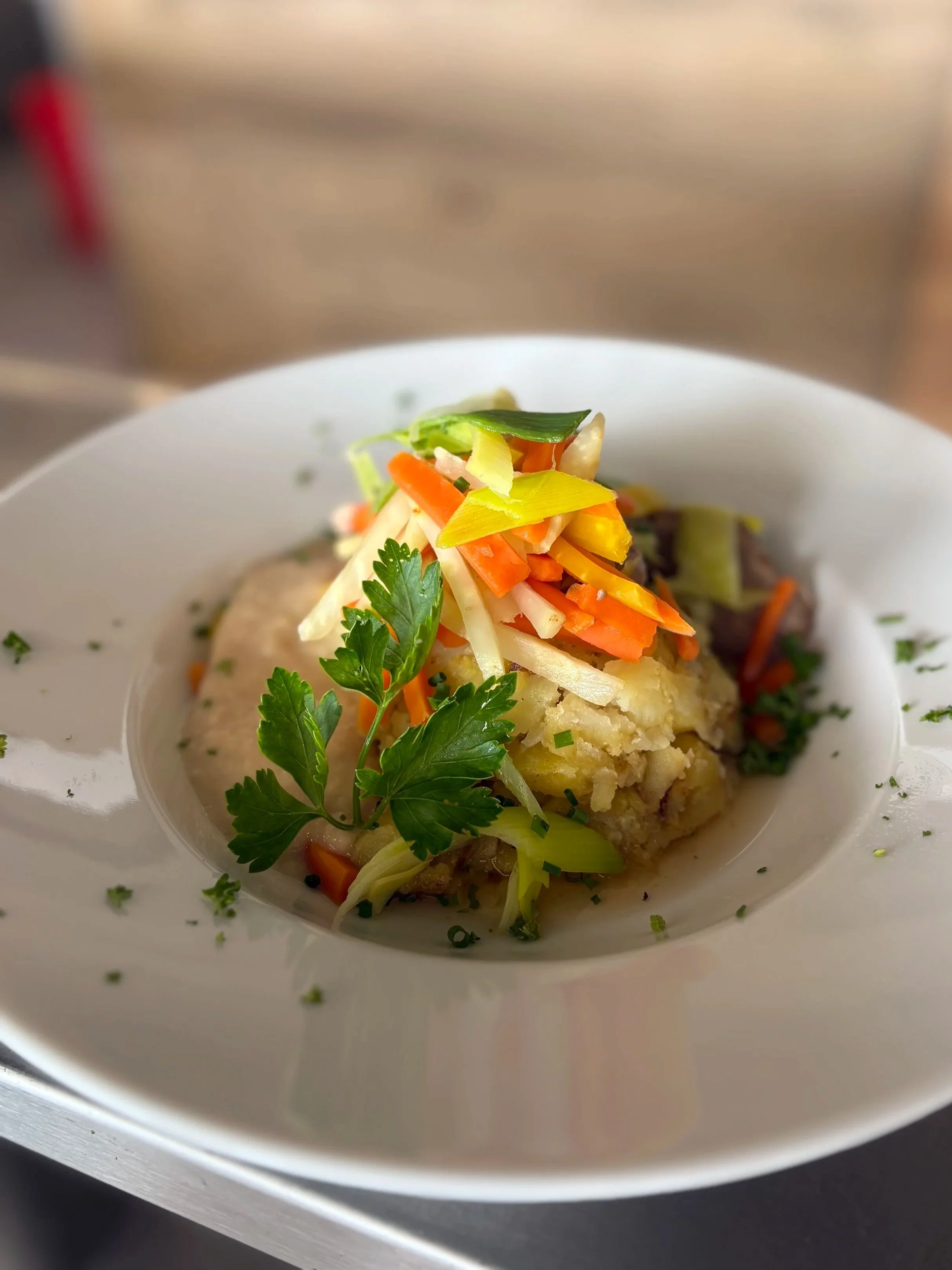 A dish with mashed potatoes topped with shredded vegetables, garnished with fresh parsley and herbs, served on a white plate.