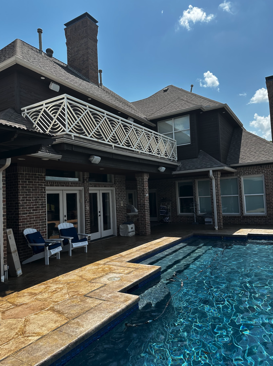 Backyard with swimming pool, patio chairs, and a two-story brick house with a balcony and multiple windows