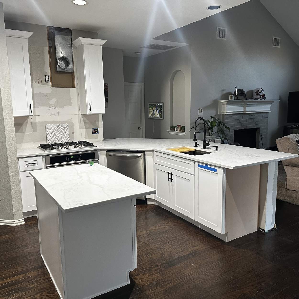 Kitchen with white cabinets, white marble countertops, a small island, stainless steel appliances, and a double sink with a black faucet.