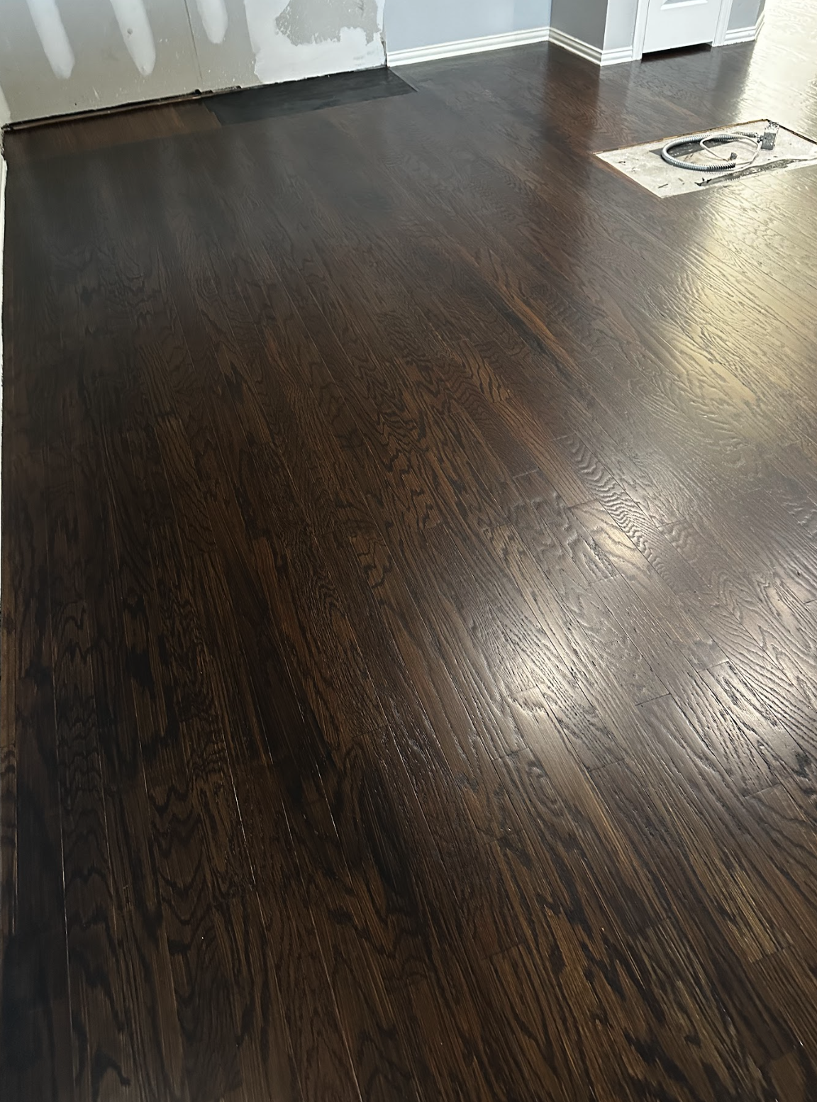Finished dark wood floor installation in a room with drywall and an electrical outlet cutout.