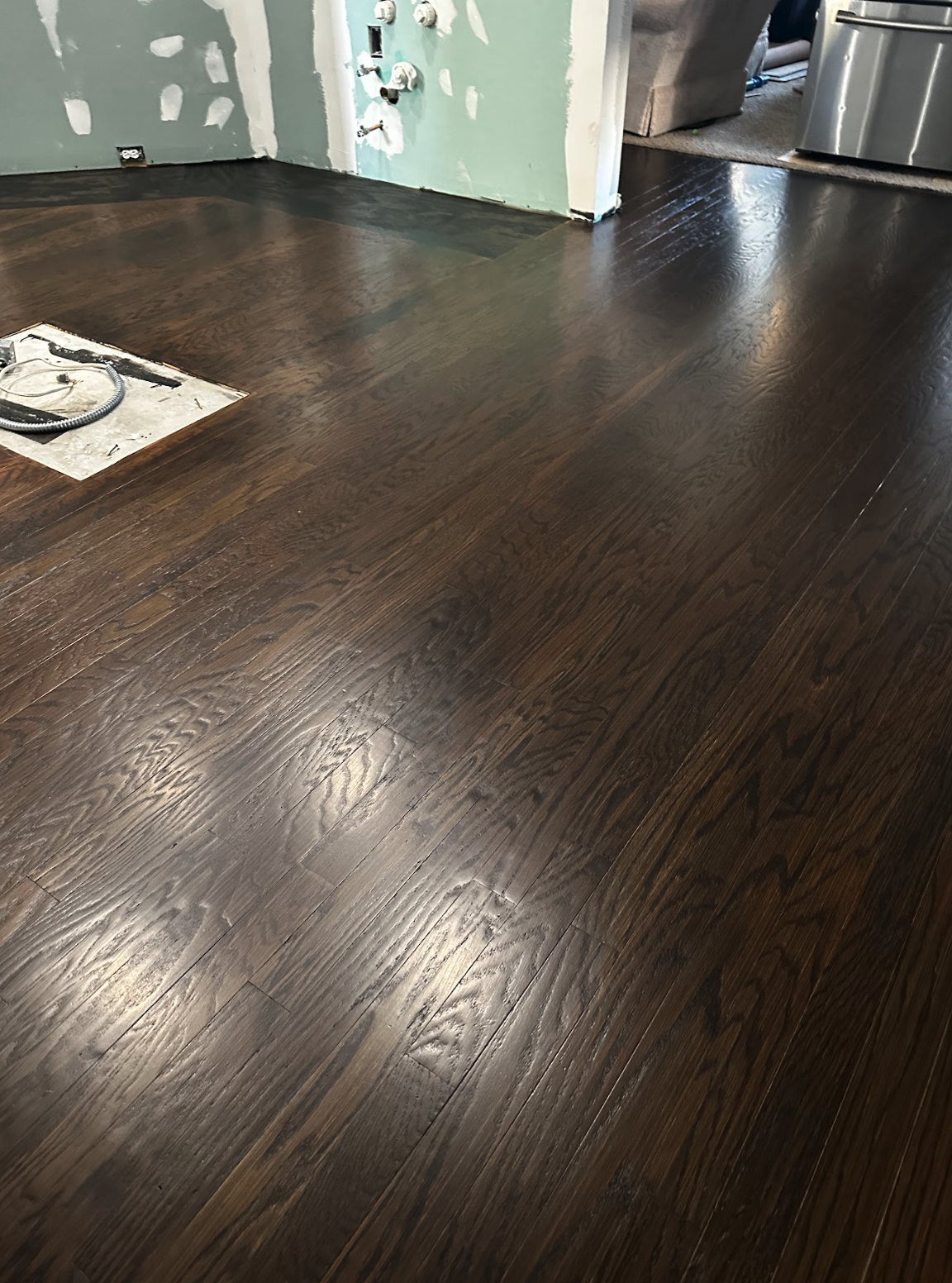 Finished dark hardwood flooring in a room with an opening for an electrical outlet and wires.