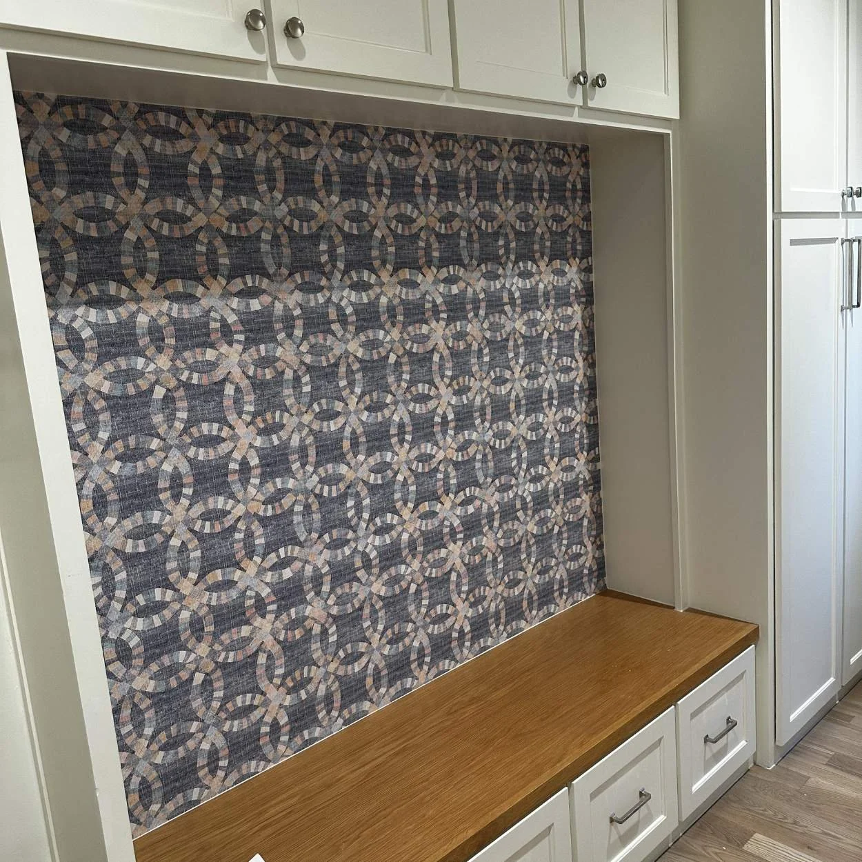 Built-in cabinet with a patterned textile backing and a wooden bench below, in a kitchen or dining area.