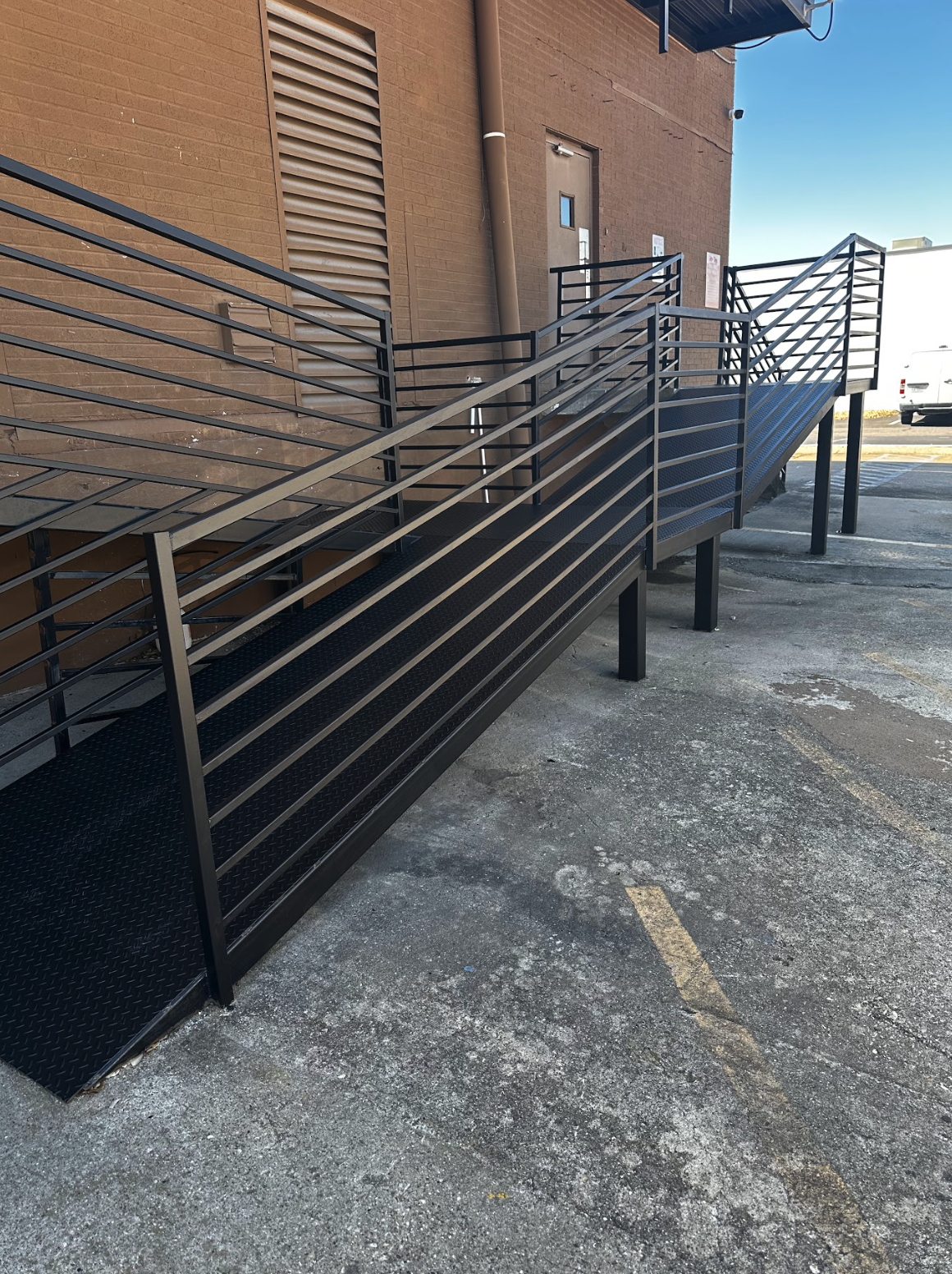 A black metal fire escape stairway with railings outside a brick building, leading to a door.