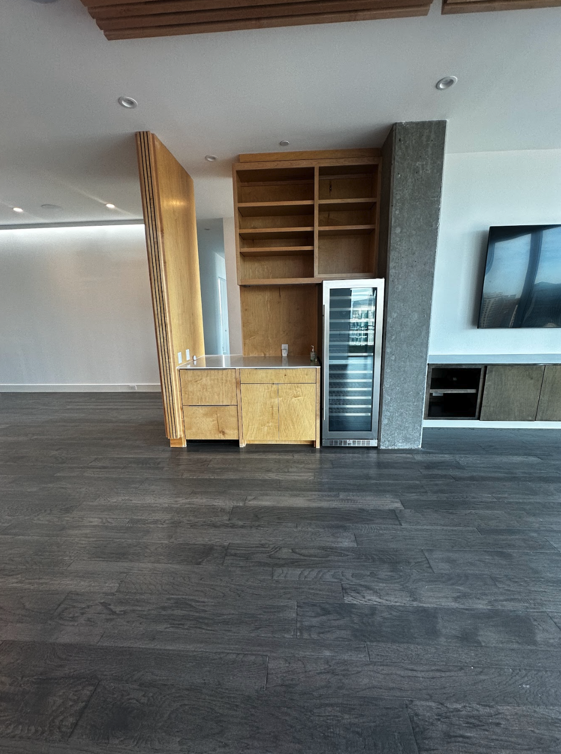 Part of a modern living room with wooden flooring, a built-in wall unit, and a glass-door wine cooler.